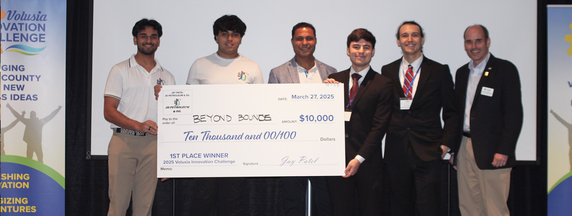 Group photo of people and 1st place winners and founders of Beyond Bounds Studios holding a big check in the amount of $10,000.